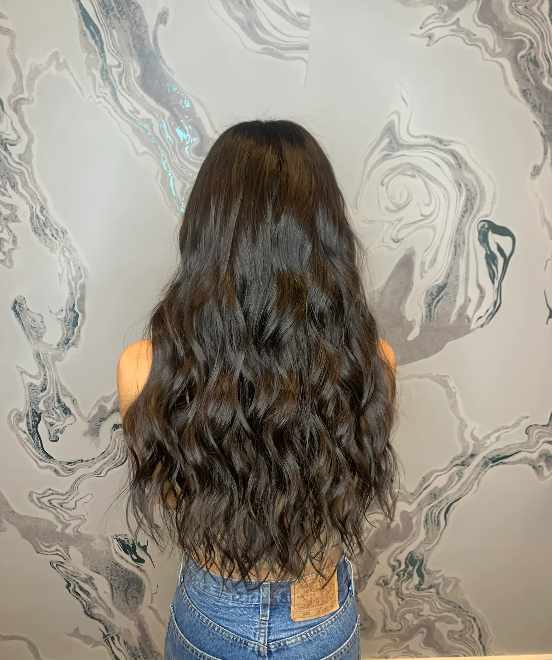 Full-length brunette hair extensions with a soft wave, photographed from behind